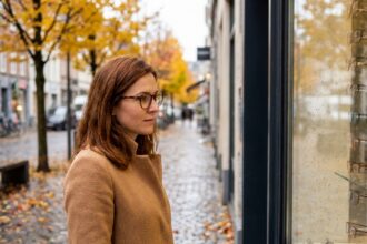 Femme portant des lunettes en écaille de tortue et un manteau camel dans une rue parisienne aux feuilles dorées en automne
